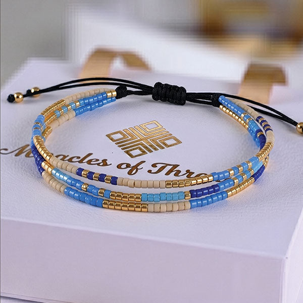 Handmade layered Miyuki bead bracelet in blue, ivory, and gold tones with adjustable cord closure and 24K gold plated beads