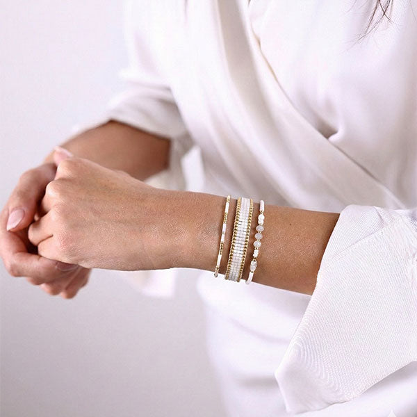 Set of three handmade Miyuki bead bracelets in ivory and gold tones with 24K gold plated beads worn stacked on wrist