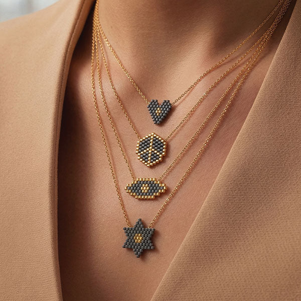 Layered handmade Miyuki bead necklaces with heart, shield, eye, and star pendants in grey and gold tones with 24K gold plated beads