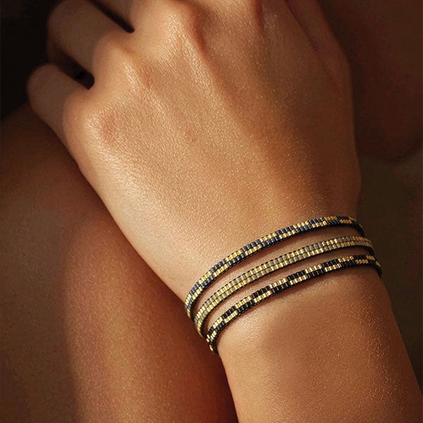 Handmade Miyuki bead bracelet in gold with black, blue, and green color variations layered on wrist with 24K gold plated beads