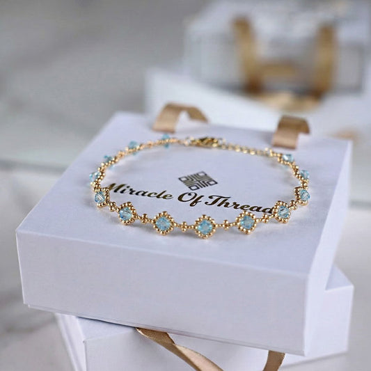 Aqua blue crystal bracelet with 24K gold plated chain and halo station design displayed on luxury jewelry box