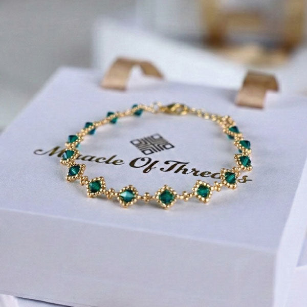 Emerald green crystal bracelet with 24K gold plated chain and halo station design displayed on luxury jewelry box