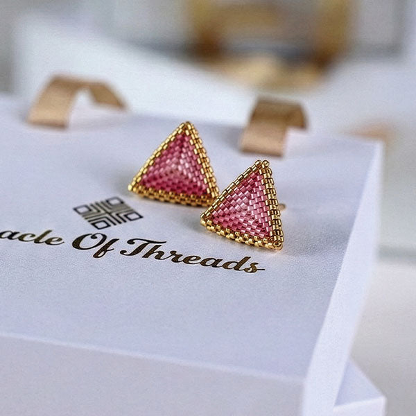 Handmade rose pink Miyuki triangle earrings with 24K gold plated detailing displayed on luxury jewelry box