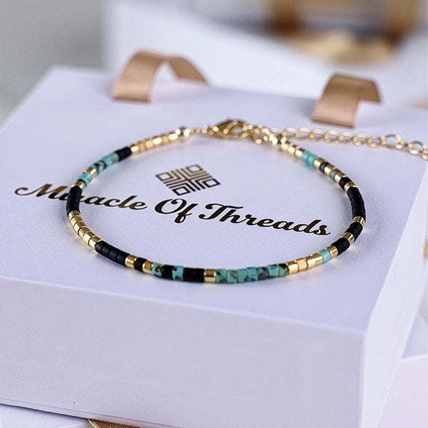 Handmade Miyuki bead anklet in black, turquoise, and gold tones with 24K gold plated beads displayed on jewelry box