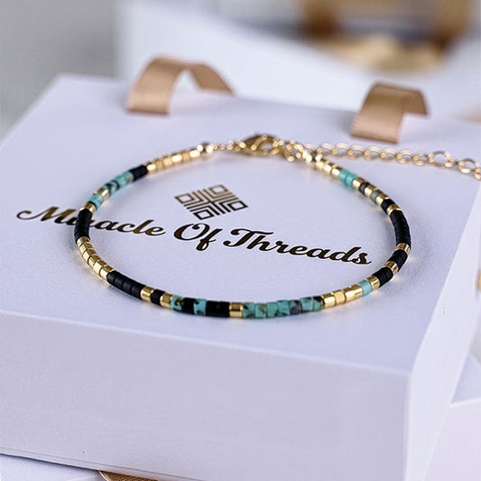 Handmade Miyuki bead anklet in black, turquoise, and gold tones with 24K gold plated beads displayed on jewelry box
