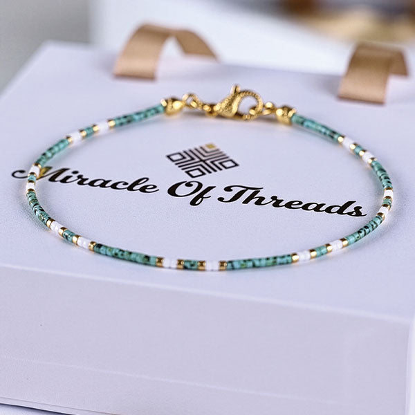 Handmade Miyuki bead anklet in turquoise, white, and gold tones with 24K gold plated beads displayed on jewelry box