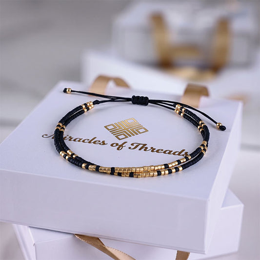 Handmade black and gold Miyuki bead bracelet with adjustable cord closure and 24K gold plated beads displayed on jewelry box