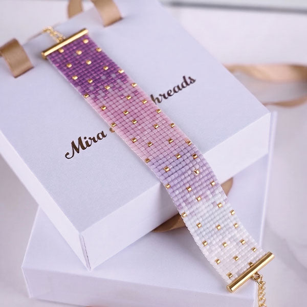 Handmade Miyuki bead bracelet with ivory and lavender ombré pattern and 24K gold plated bead accents displayed on jewelry box
