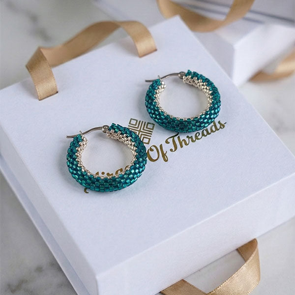 Handmade emerald green Miyuki bead hoop earrings with silver accents displayed on luxury jewelry box