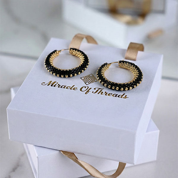 Handmade black Miyuki bead hoop earrings with 24K gold plated beads displayed on luxury jewelry box