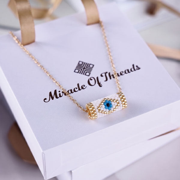 Handmade Miyuki bead necklace with blue eye pendant in ivory and gold tones featuring 24K gold plated beads
