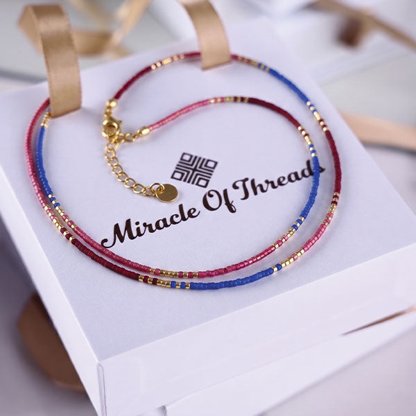 Handmade Miyuki bead necklace in berry pink and blue tones with gold accents and 24K gold plated beads displayed on jewelry box