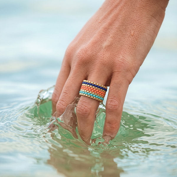 Handmade Miyuki bead ring in turquoise, peach, coral, and blue tones with 24K gold plated beads displayed on jewelry box
