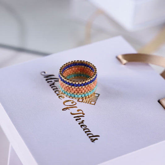 Handmade Miyuki bead ring in turquoise, peach, coral, and blue tones with 24K gold plated beads displayed on jewelry box