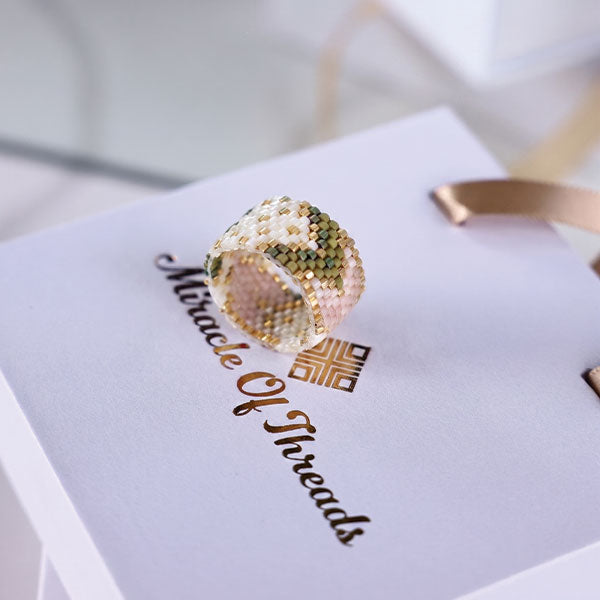 Handmade Miyuki bead ring in ivory and olive green floral geometric pattern with 24K gold plated beads displayed on jewelry box