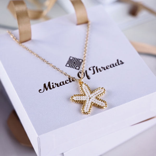 Handmade Miyuki bead starfish necklace and earrings set in ivory and gold tones with 24K gold plated elements worn on beach