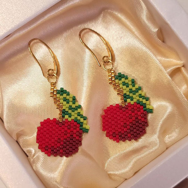 Handmade cherry-shaped Miyuki bead earrings in red and green with 24K gold plated hooks displayed on silk background