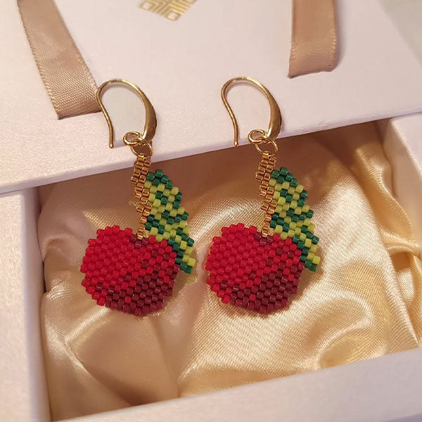 Handmade cherry-shaped Miyuki bead earrings in red and green with 24K gold plated hooks displayed on silk background