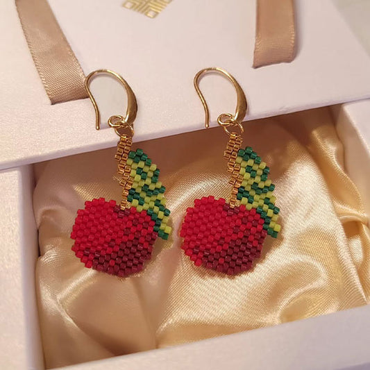 Handmade cherry-shaped Miyuki bead earrings in red and green with 24K gold plated hooks displayed on silk background