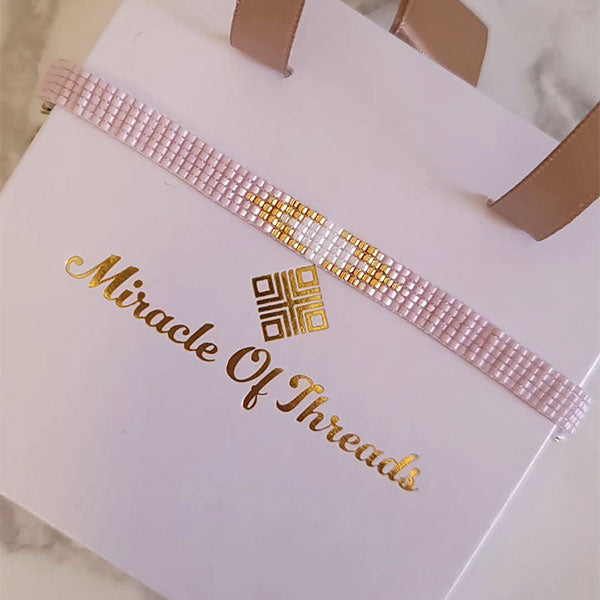 Handmade blush Miyuki bead bracelet with central gold detail and 24K gold plated beads displayed on gift box